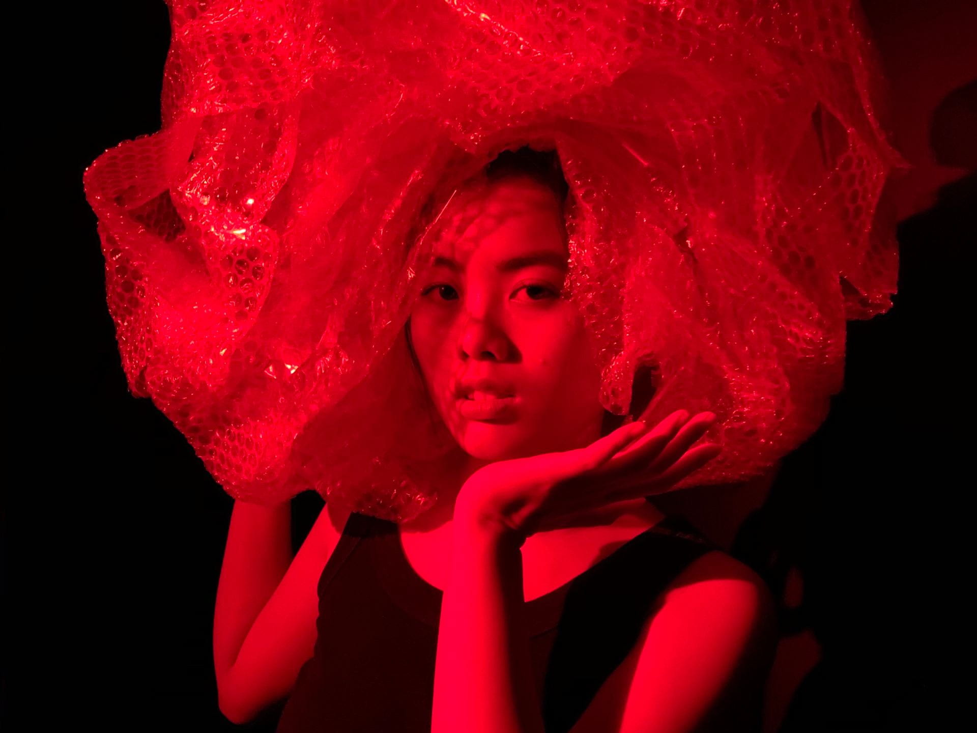 Model wearing a bubble-wrap wig under red light.
