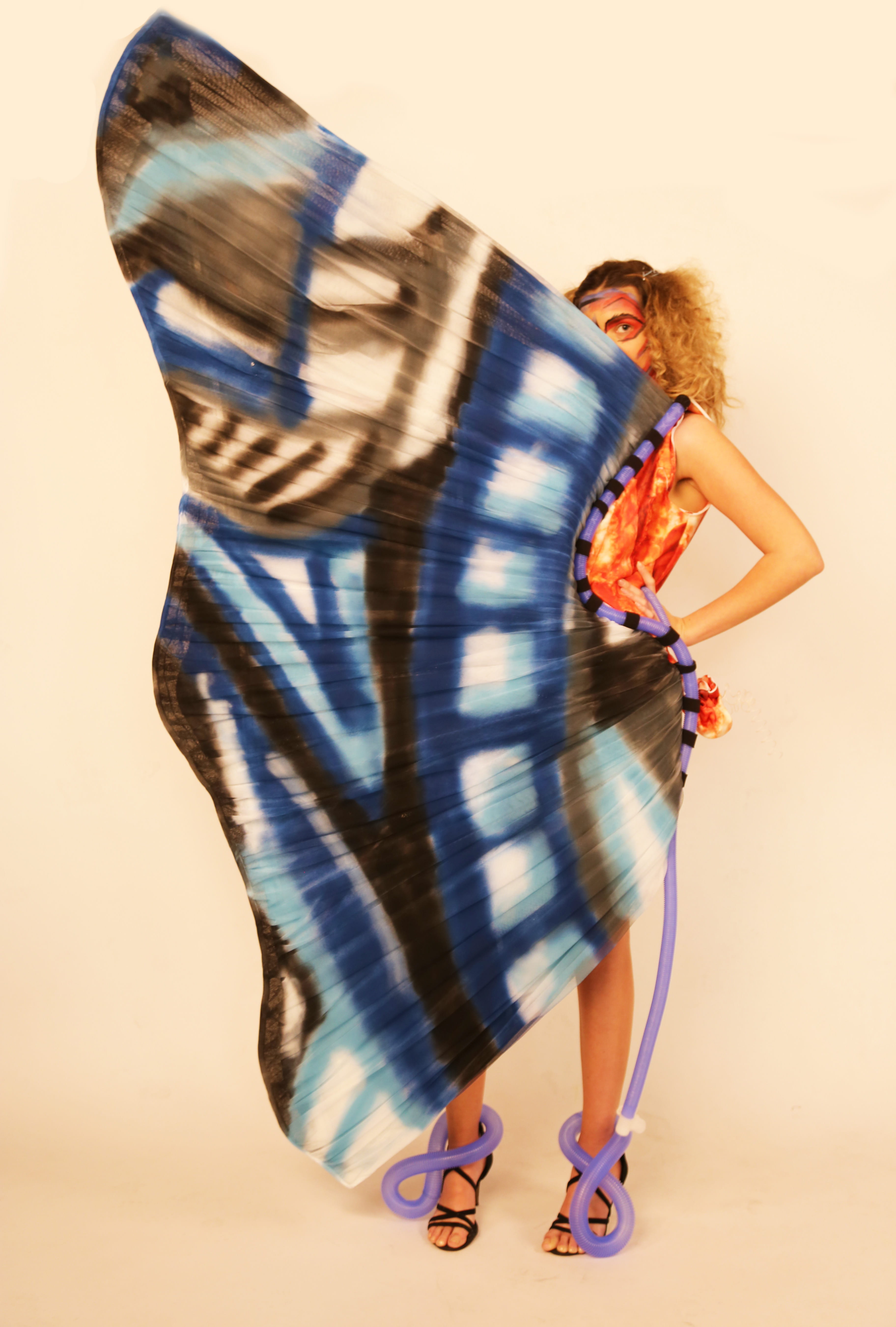 A female model in a red and yellow, meat-themed dress, behind a large, blue butterfly wing.