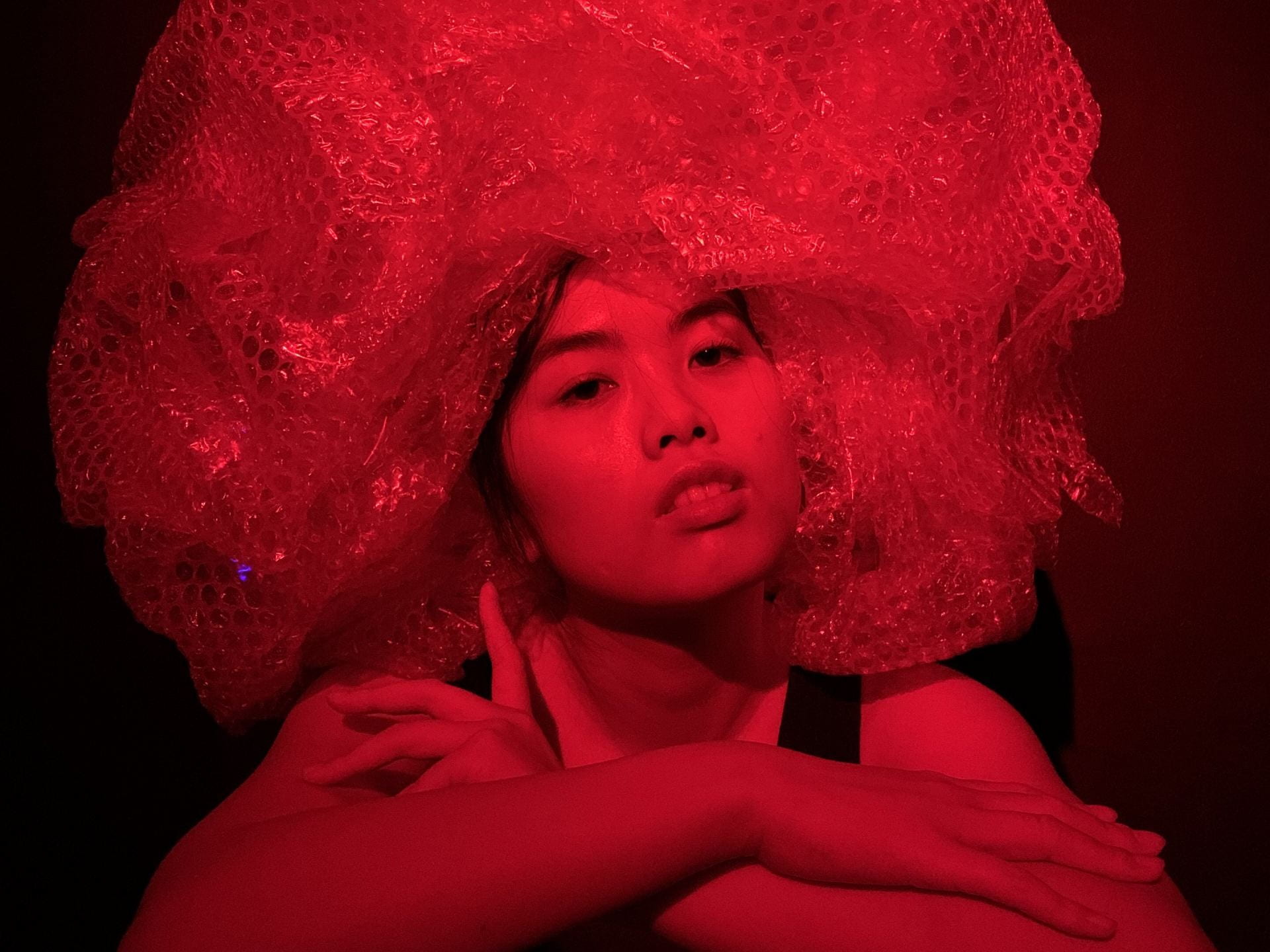 Model wearing a bubble-wrap wig under red light.