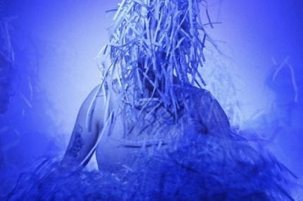 A blue tone image of a person with shredded paper on their head as though its hair.