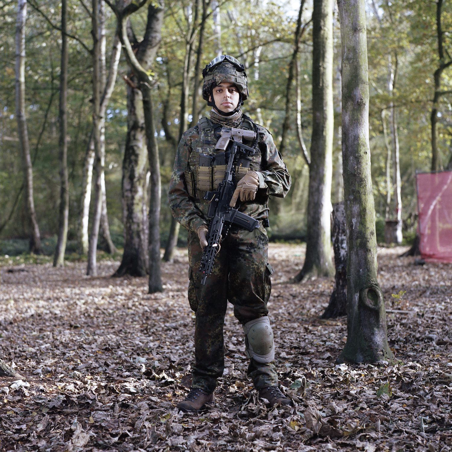 A young man wearing Russian camouflage stands in front of the camera, with a toy rifle slung against his chest.