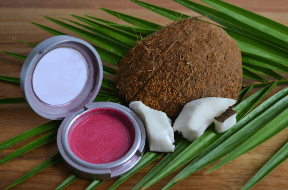 The ChemoCosmetics blusher, next to a coconut and placed on top of of a palm frond.