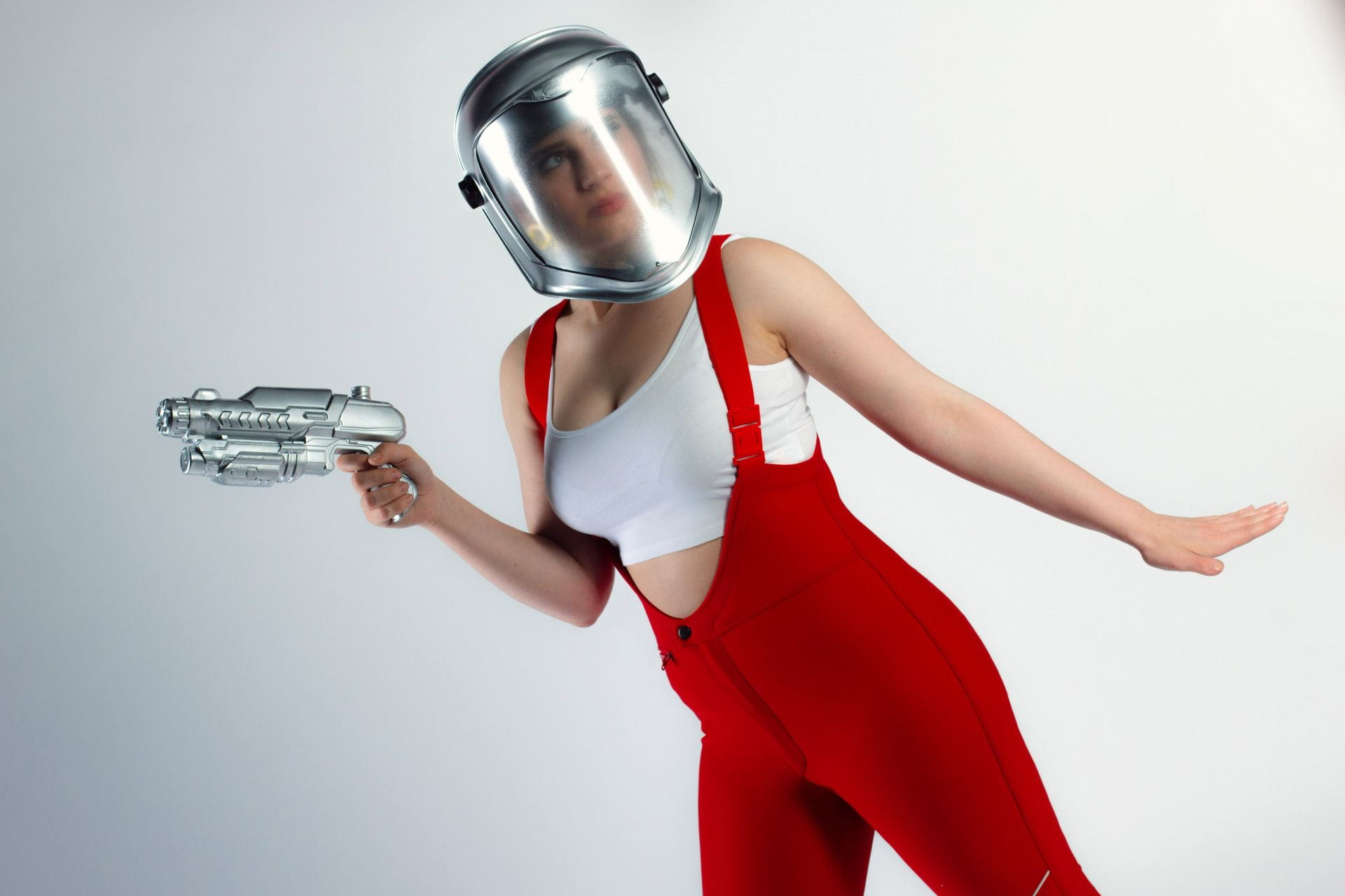 A woman in red dungarees and wearing a gas-mask, holding up a silver laser-gun.