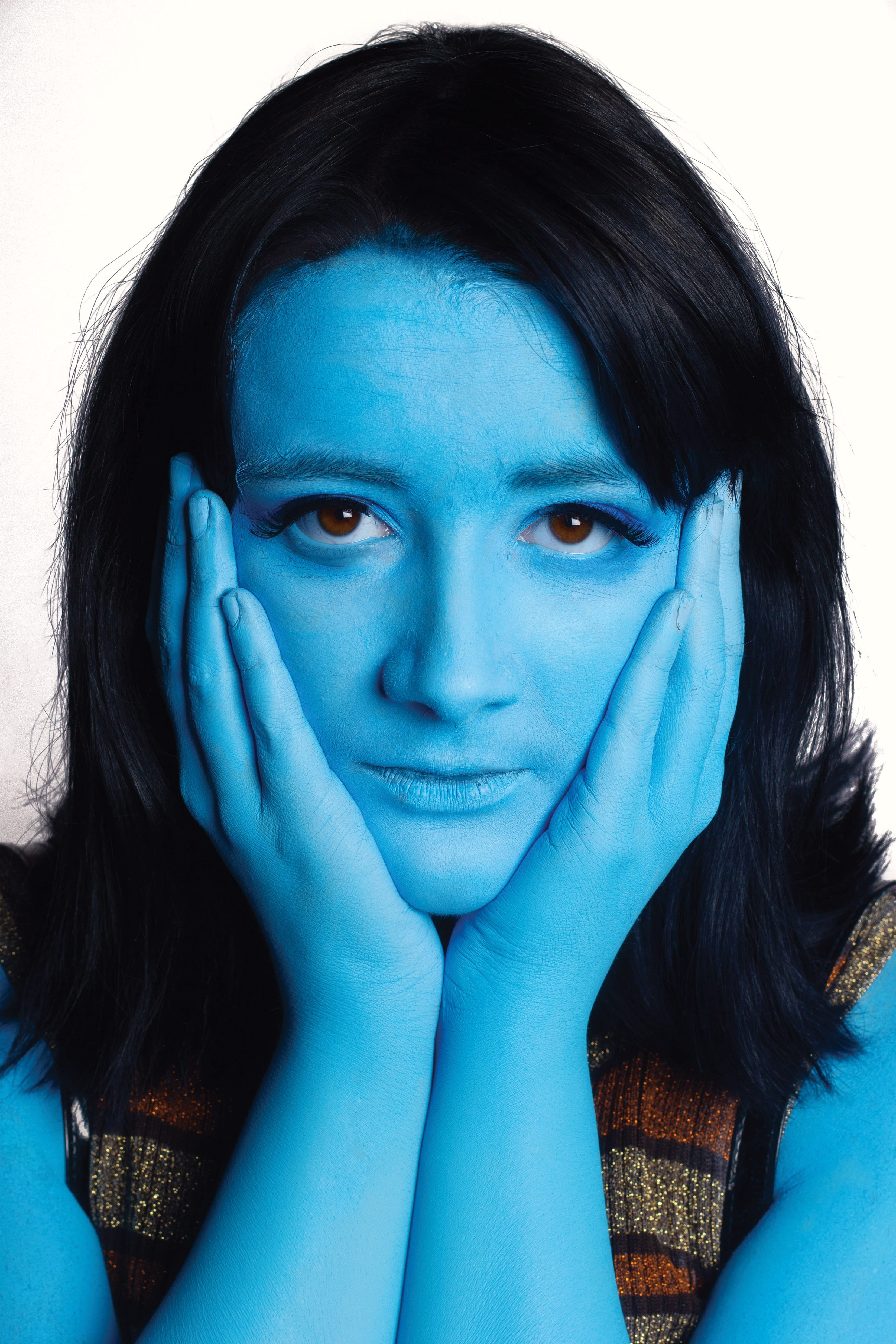 A woman with blue skin, placing her palms on her cheeks.