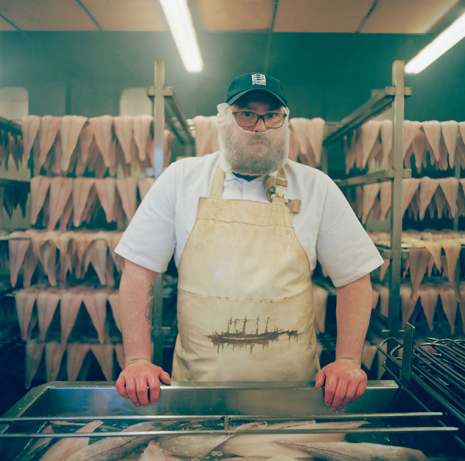 A fishmonger standing over a large tub of fish. 