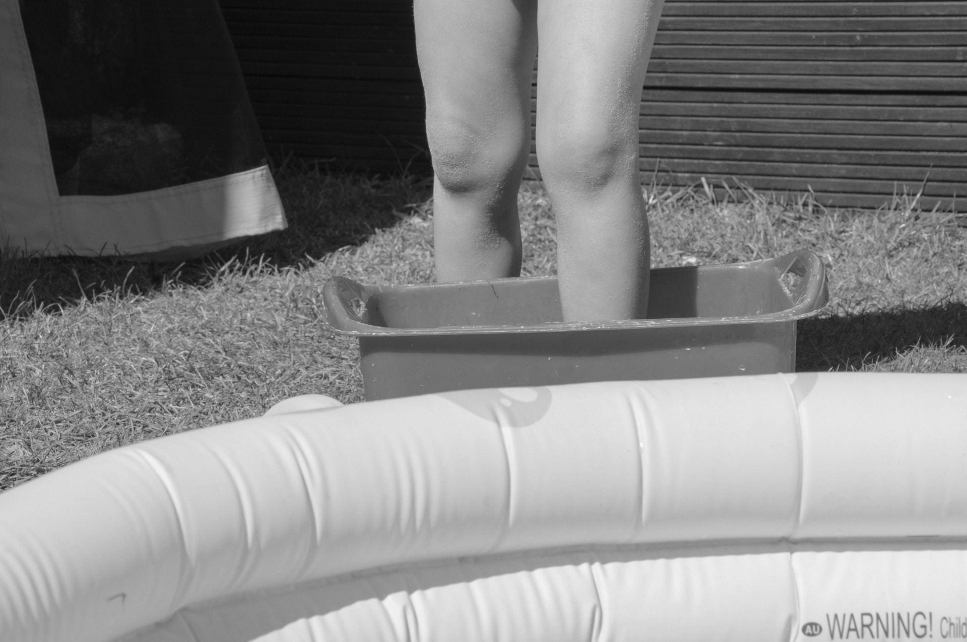 Black and white photograph of a child by a paddling pool.