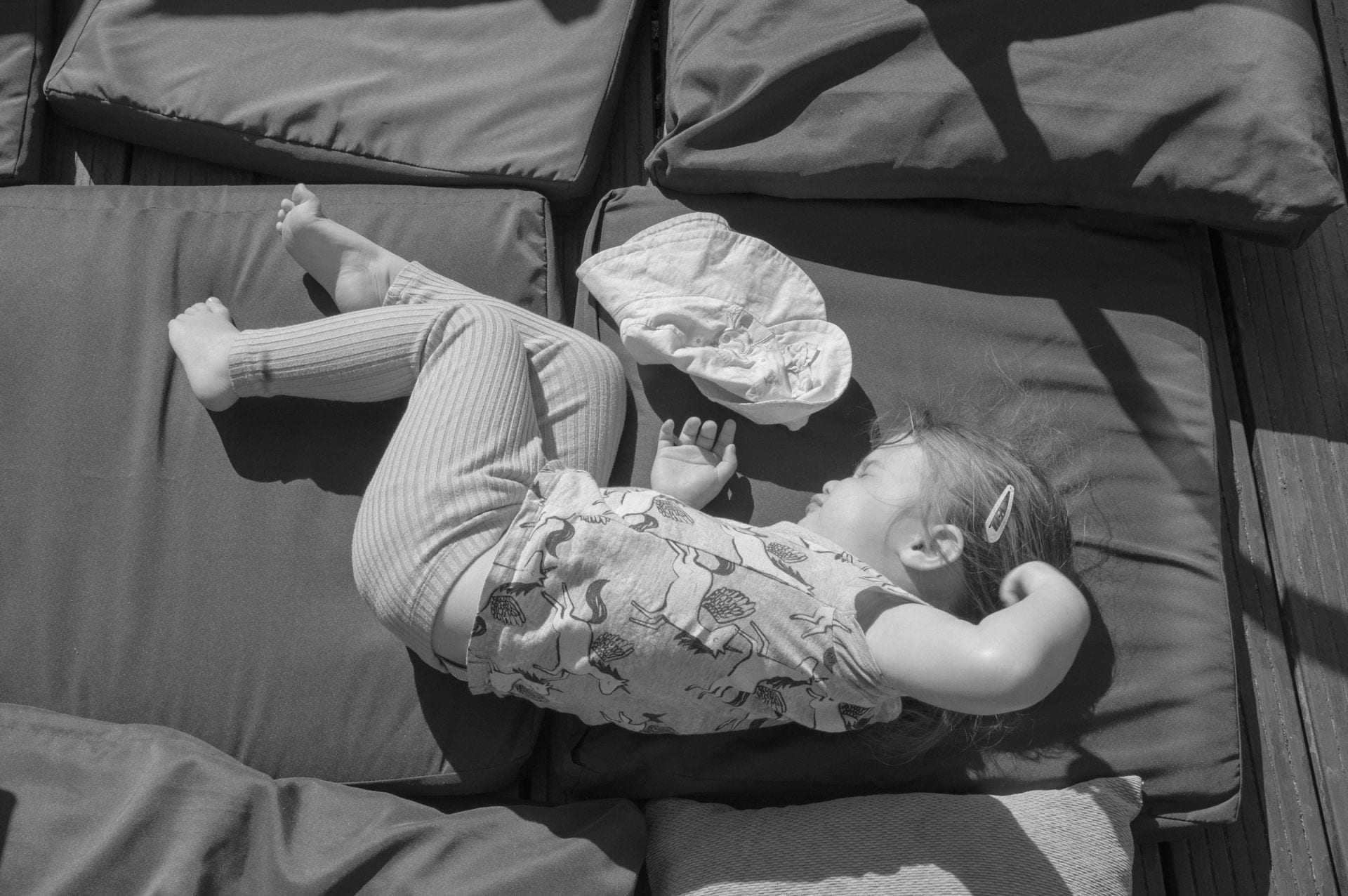 Black and white photograph of a child asleep on garden cushions.