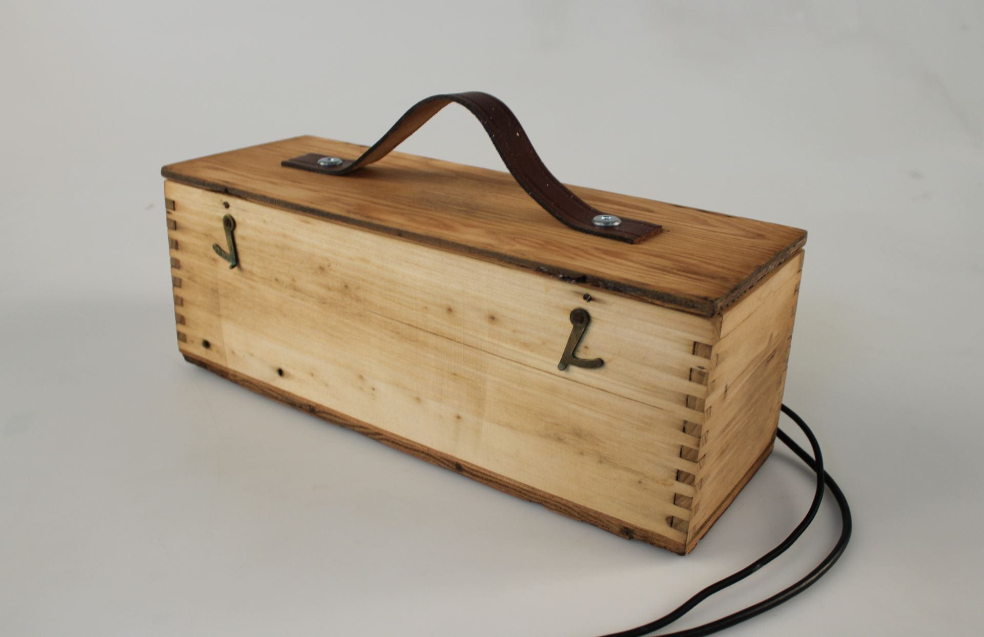 A rustic wooden box, with a leather strap on the lid, and wires at it's side.