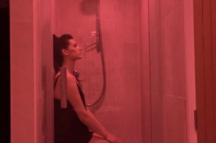 Photograph of woman leaning in shower with a pink tint