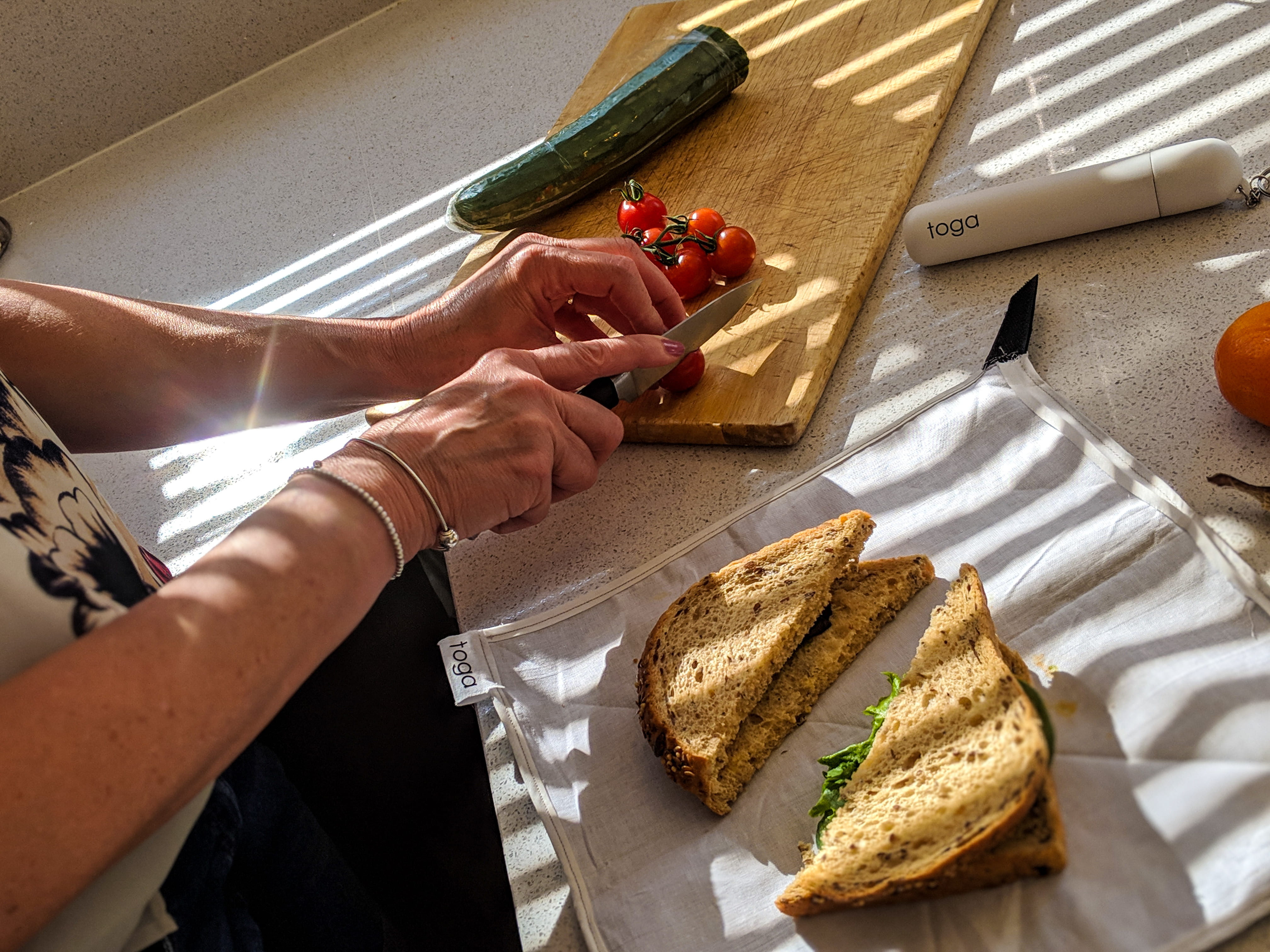 Vegetables being cut on a chopping board, with a cut sandwich and the Toga on the counter.