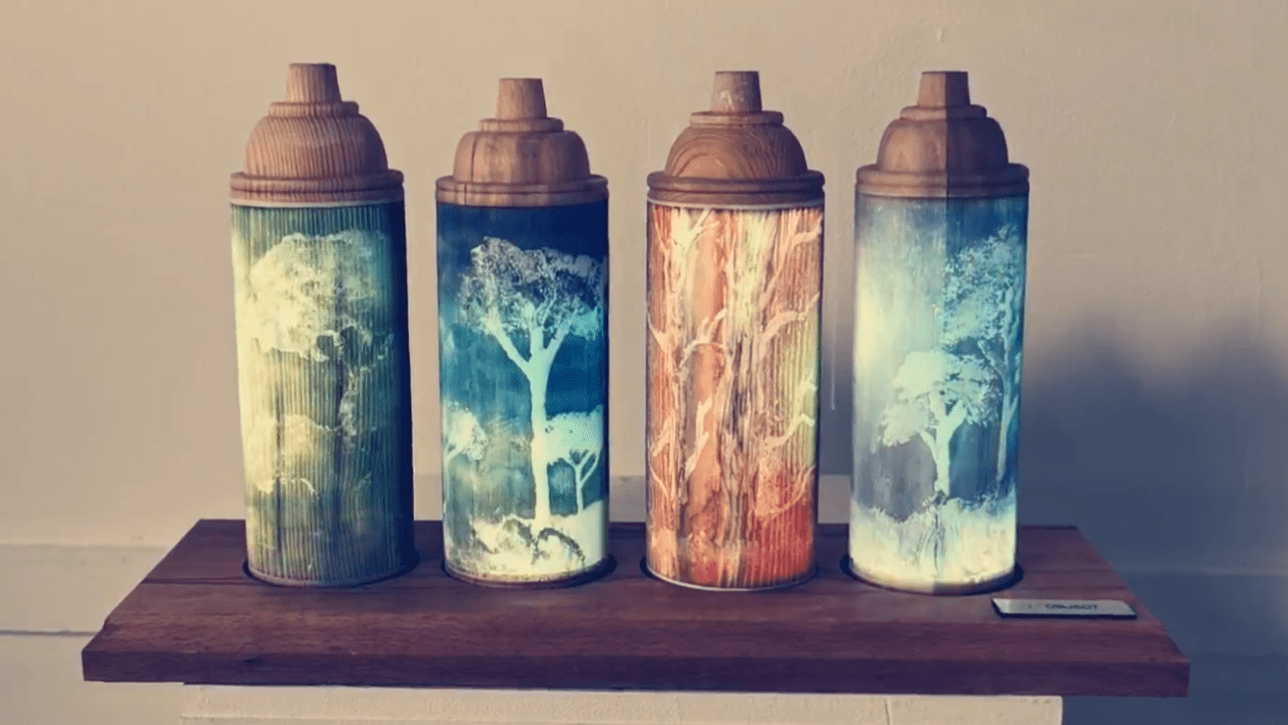 Four wooden spray paint cans on a shelf, images of tress are engraved into them, each can is a vivid colour.