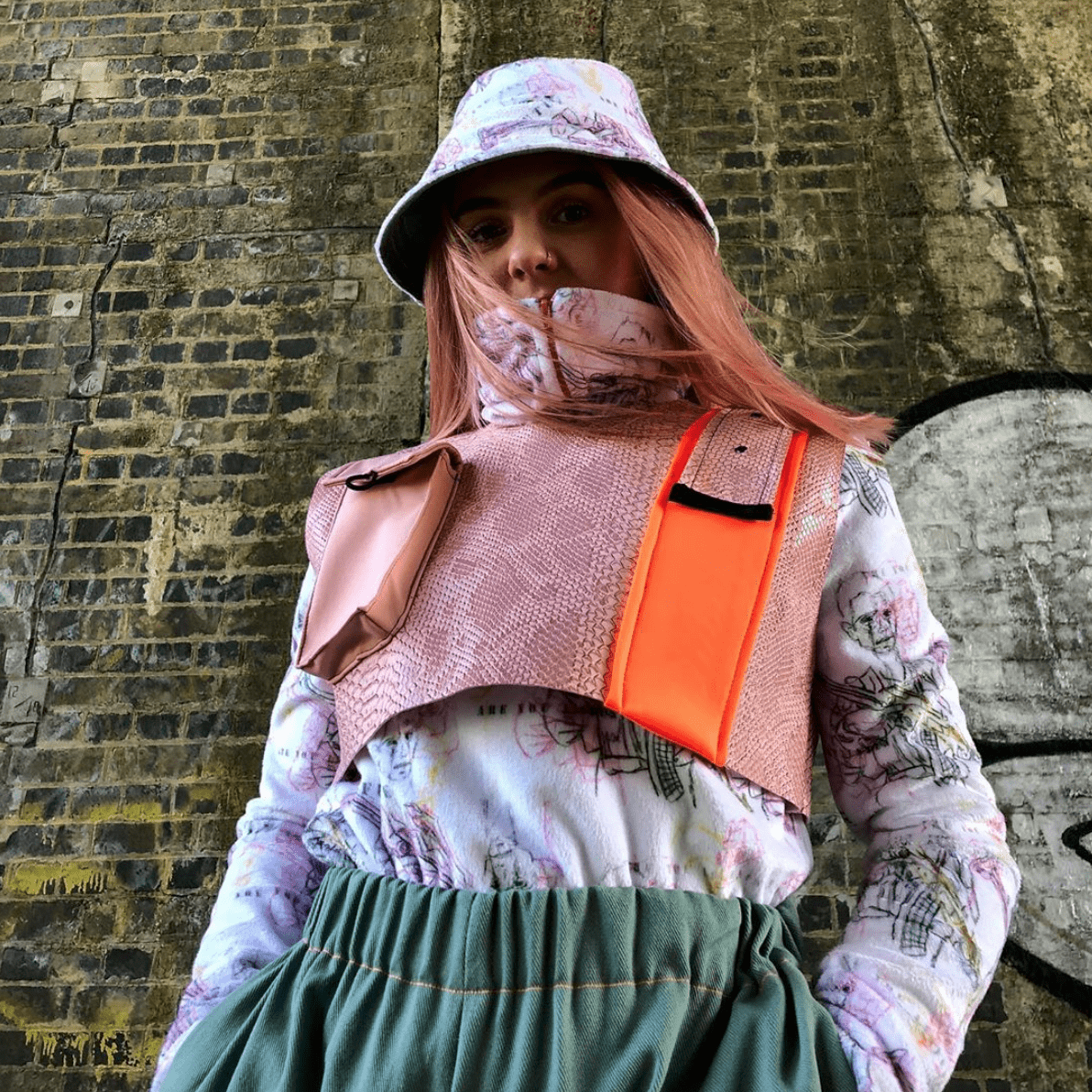 Model wearing a pink and white outfit standing next to a brick wall.