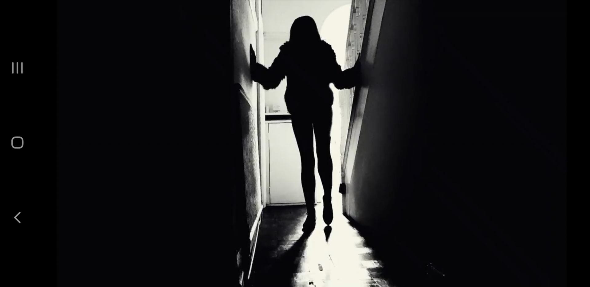 Black & white image of a person walking down a hallway. 