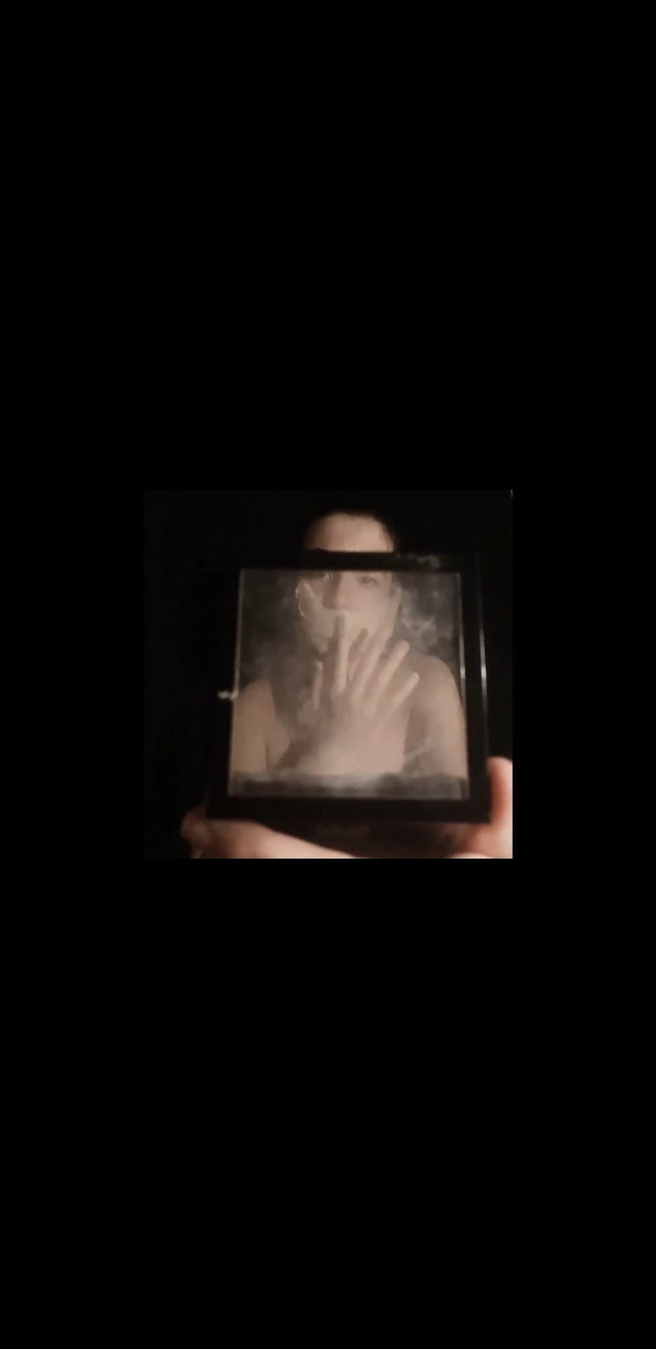 Someone holding their hand in front of their face, shot through a piece of glass.