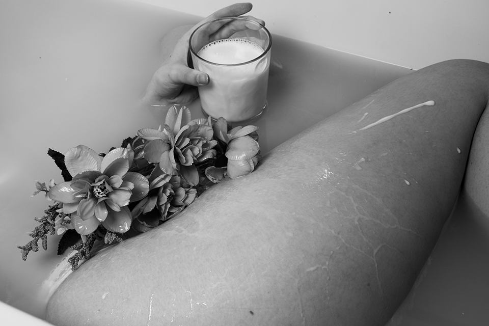 Image of a women's body in a milky bath holding a glass of milk with some fake flowers