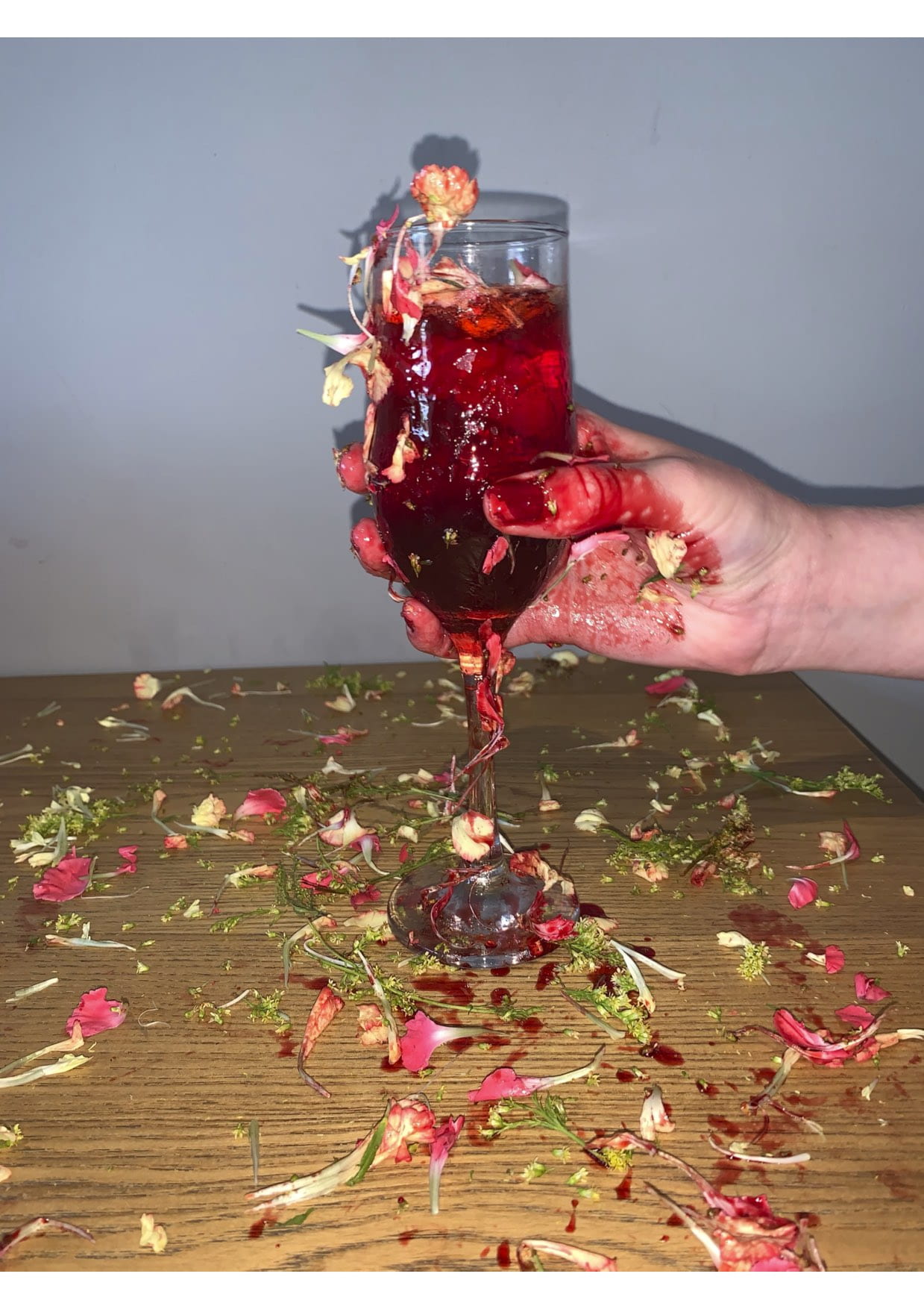 Hand holding a glass full of flowers and red liquid.