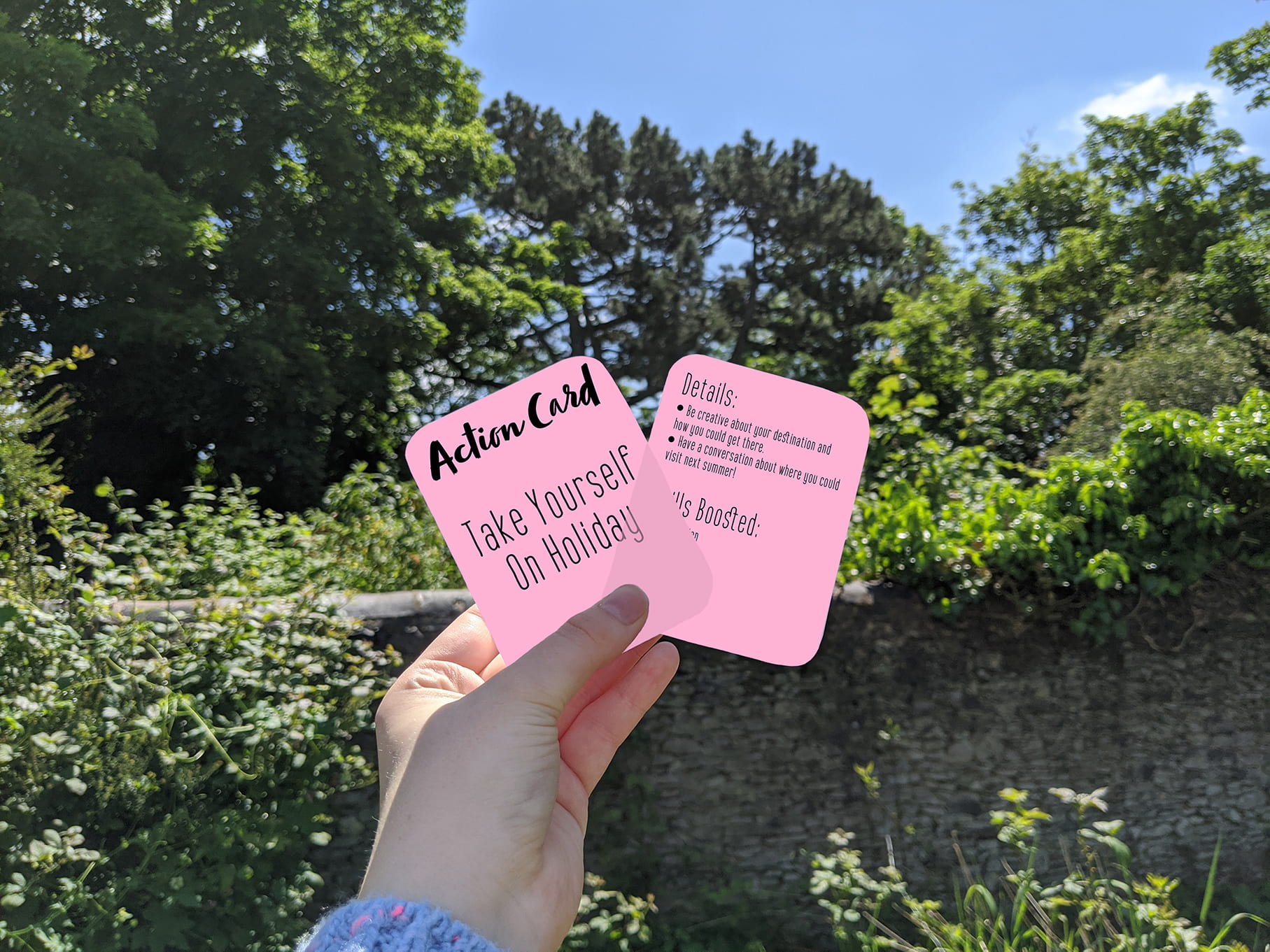 Someone holding pink cards up - These cards have an open-ended activity on the front to spark a child's imagination and relieve boredom. On the back is further detail of the activity and the skills boosted through the play.