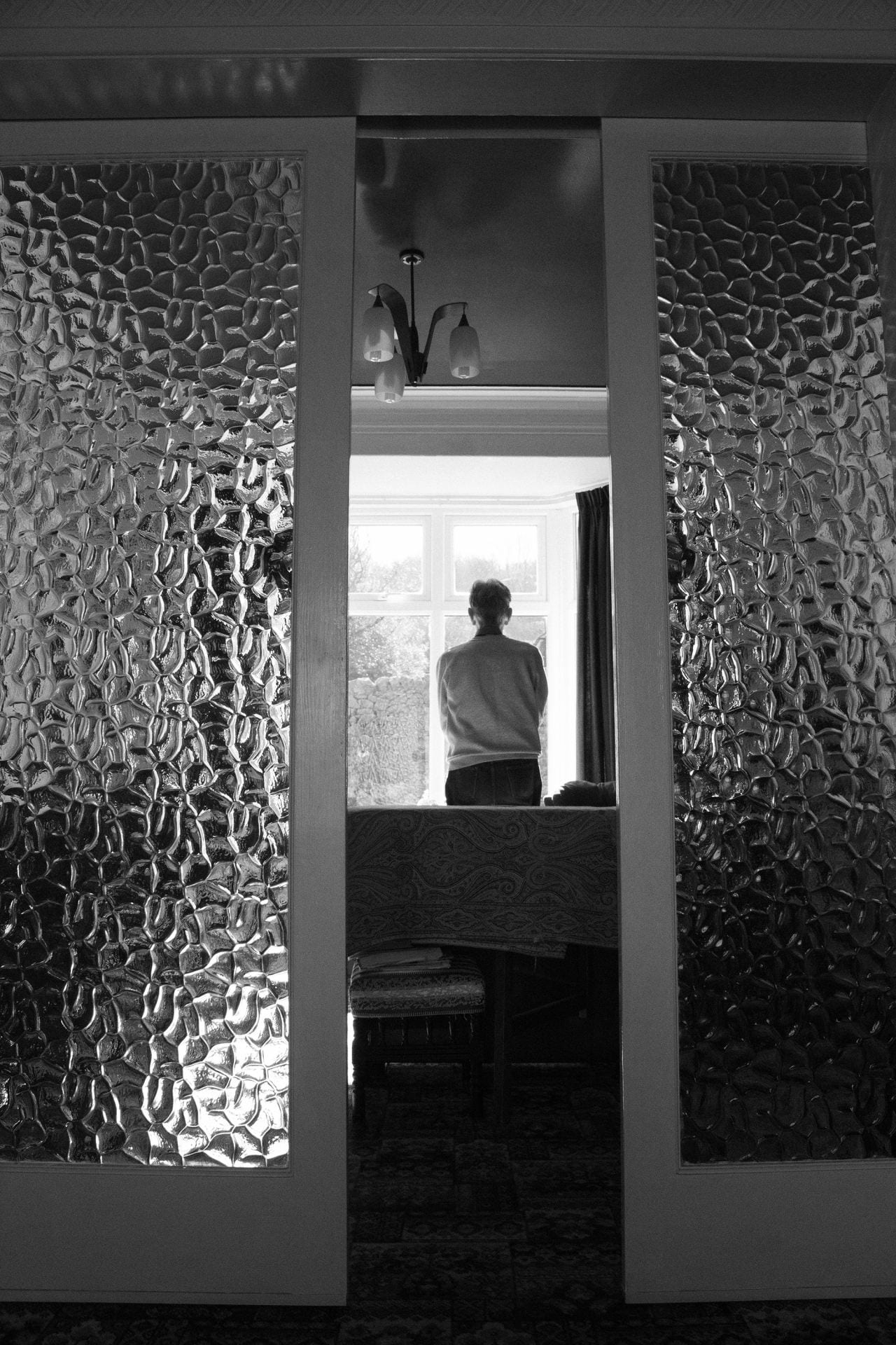 Black and white photograph of man standing by a window.